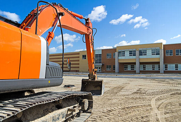 A bright orange construction excavator in the recently graded parking lot of a new high school.Similar Images: